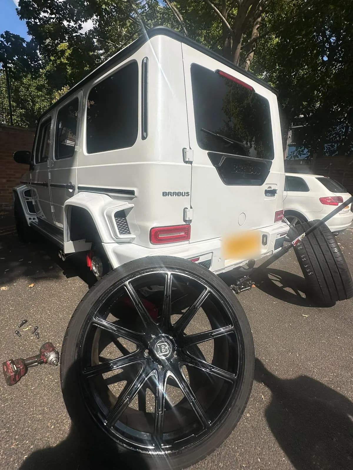 A black alloy wheel stood upright beside the rear of a white G-Class