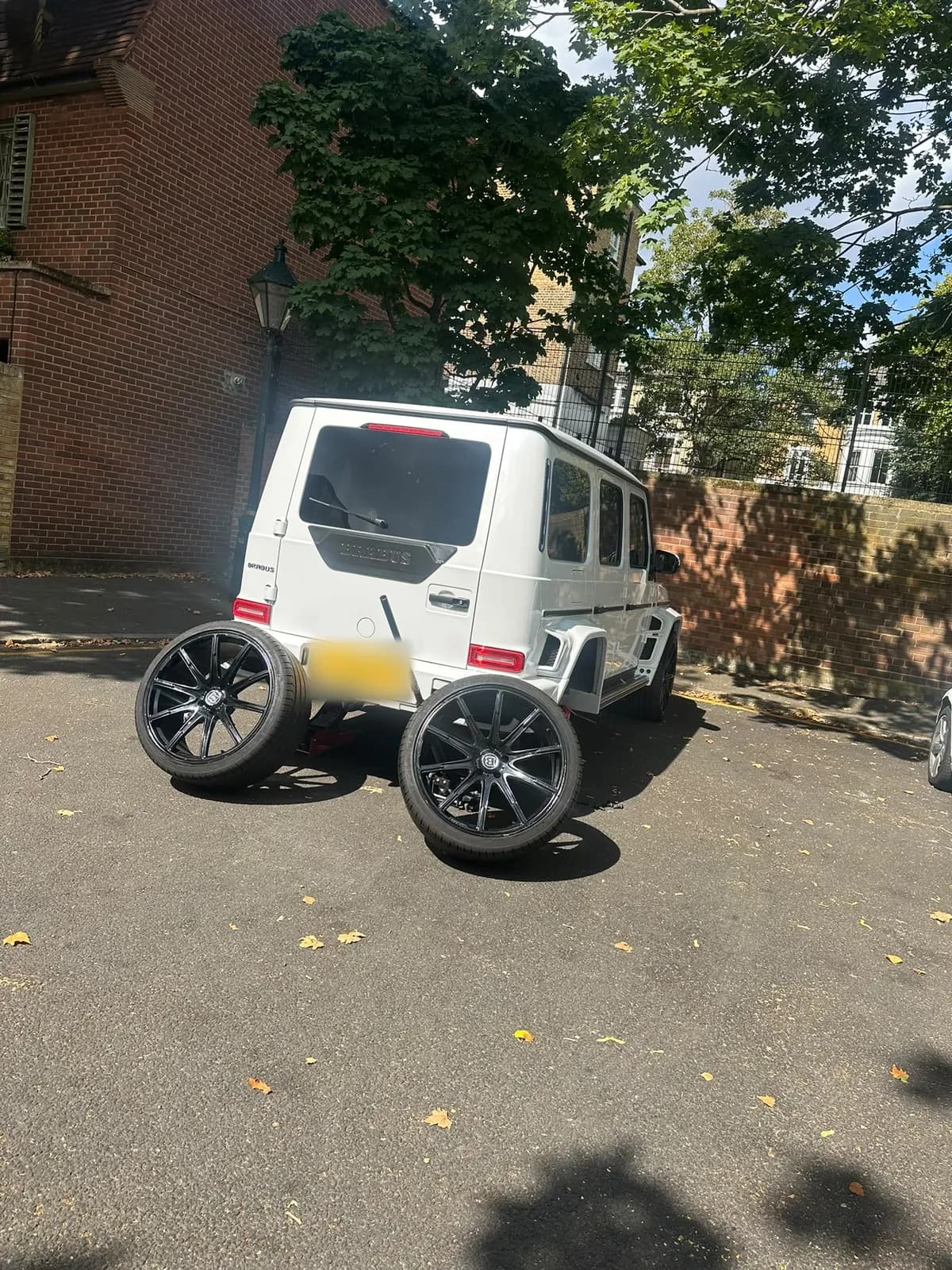 A white G-Class in a courtyard with two wheels removed and standing behind it