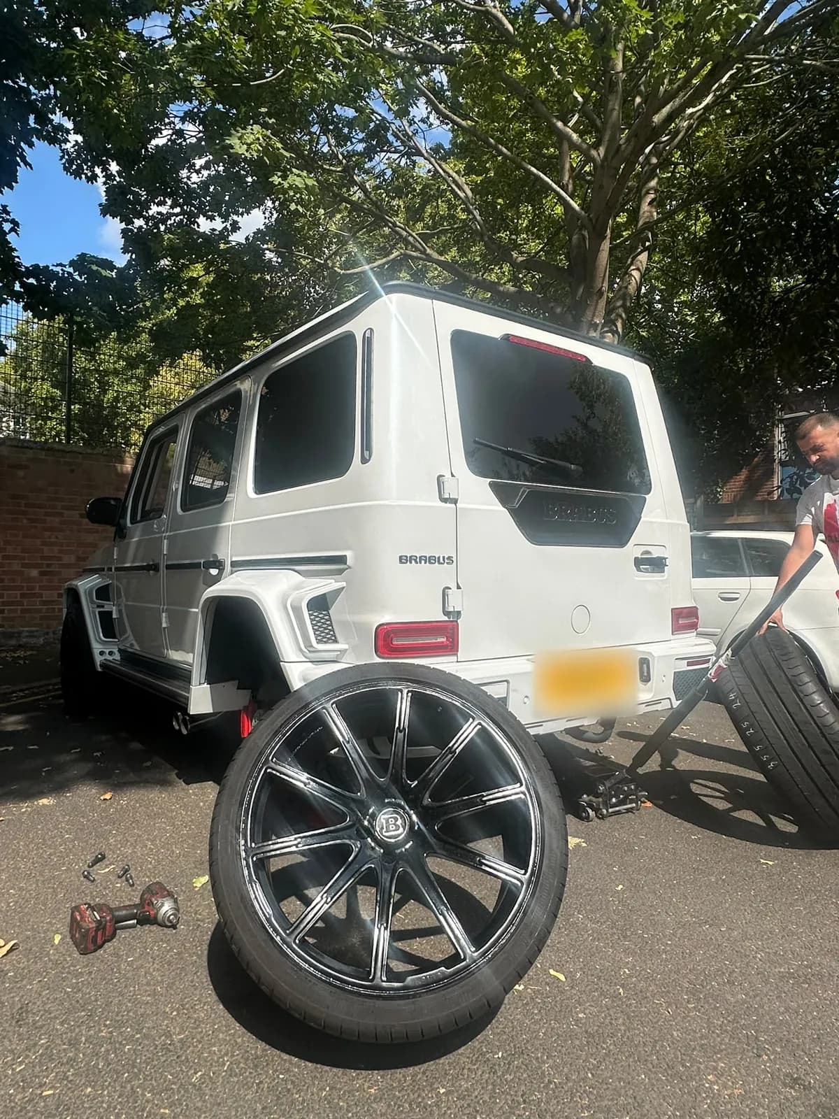 A fitter working at the side of a white G-Class with a wheel off in the foreground