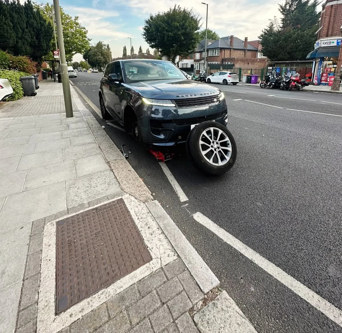 A Range Rover jacked up at the kerb with its front wheel off, leaning against the bumper
